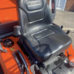 Close-up of a black Kubota tractor seat inside an orange machine.