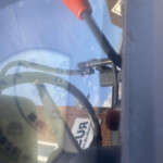 Close-up of a red lever knob connected to a black rod inside a vehicle cabin, with windshield reflections and exterior equipment visible.