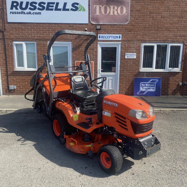 Orange Kubota riding mower parked outside a brick business with Russell's and Toro signs and a reception doorway in the background.