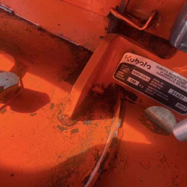 Close-up of orange industrial machinery interior with a worn metal label that reads Kubota and model/serial information nearby.