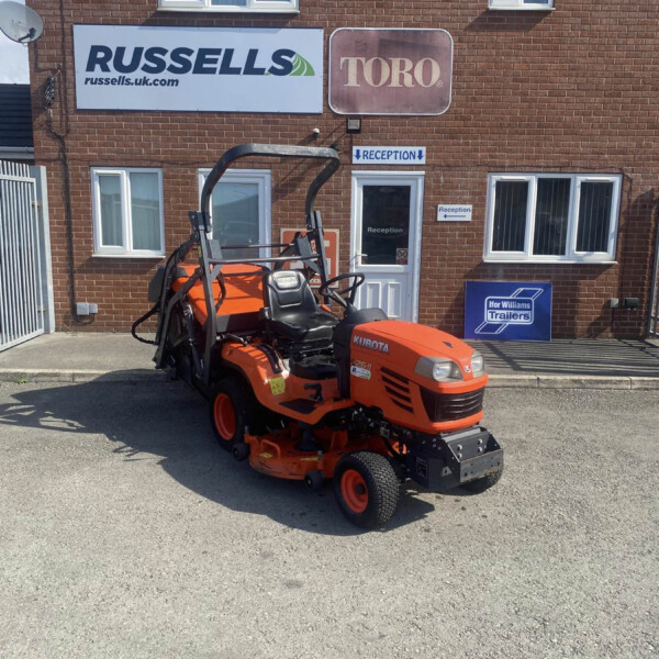 Orange Kubota ride-on lawn mower parked in front of a brick building with Russell's and Toro signs and a reception door nearby.
