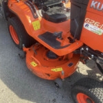 Close-up of an orange riding lawn mower deck with a black seat and pedals visible underneath the seat area