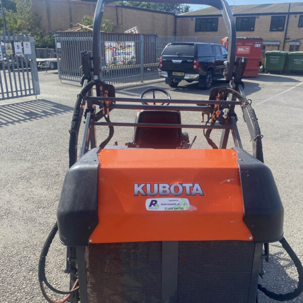 Back view of a Kubota construction vehicle with orange body, protective roll bar, and warning stickers in a parking lot.