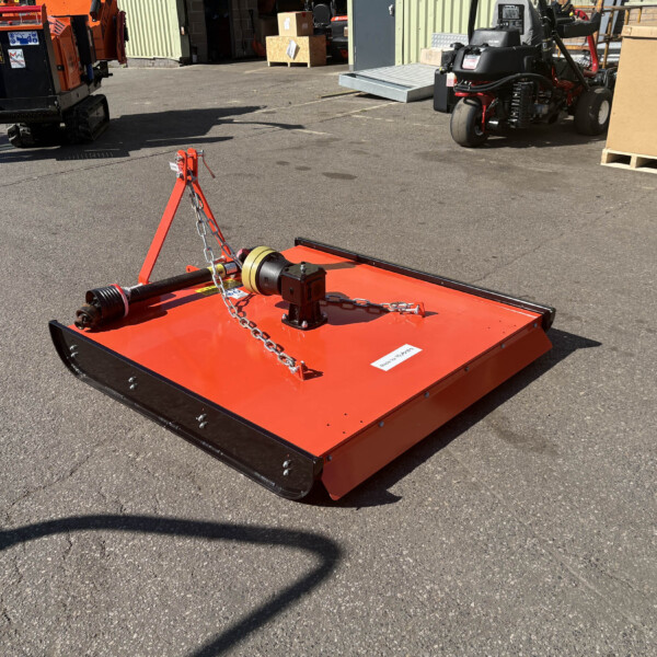 Close-up of a red/orange mower deck with chains and hitch on a paved outdoor yard surface.