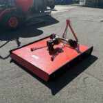 Red industrial platform with chains and lifting hardware in a yard, surrounded by machinery and pallets in the background.