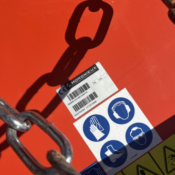 Close-up of an orange industrial surface with a white safety label and a rusted metal chain attached nearby.