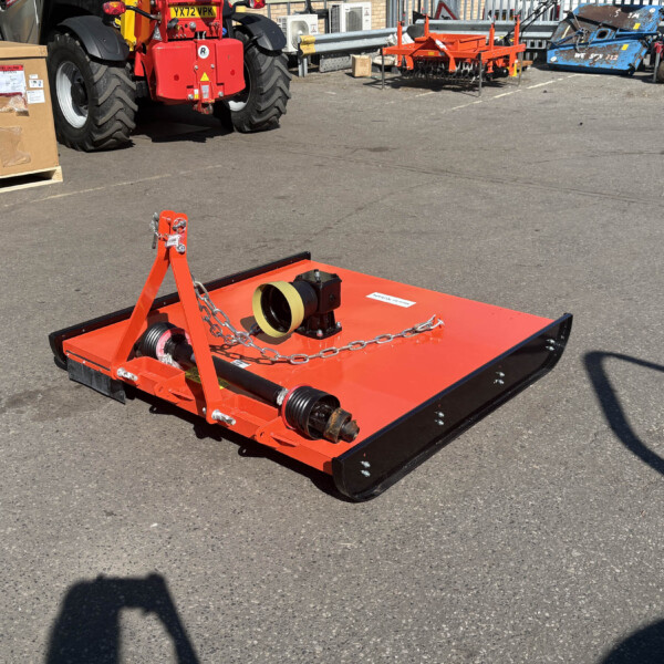 Orange heavy-duty agricultural implement with chains and rollers, placed in a paved yard with tractors and other equipment in the background.