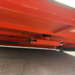 Close-up of red metal beams and rollers underneath heavy equipment on a paved surface.