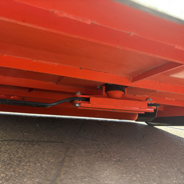 Close-up of red metal beams and rollers underneath heavy equipment on a paved surface.