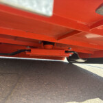 Close-up of orange metal beams and joints on industrial equipment resting on pavement.