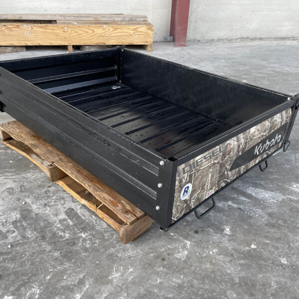 Black metal cargo bed resting on wooden pallets in a concrete, industrial space, no people visible.