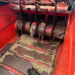 Interior view of a red agricultural baler/harvester showing rotating spiral auger cylinders and straw scattered inside the chamber.