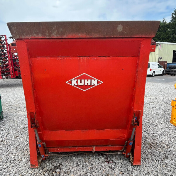 Red KUHN agricultural hopper/spreader in an outdoor equipment lot on a gravel surface, blue sky above
