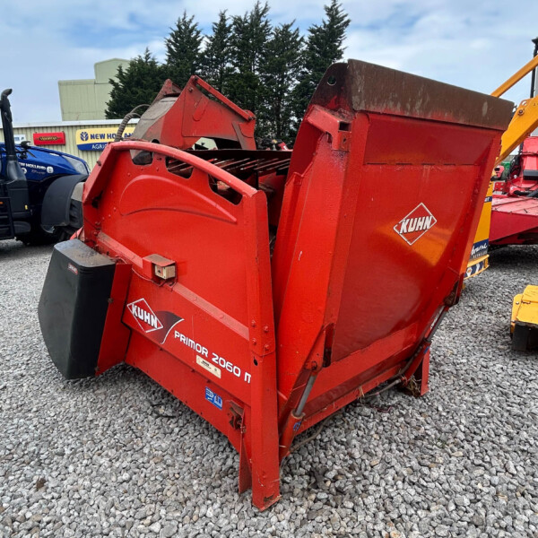 Red KUHN Primor 2060 bale wrapper on a gravel lot, with other farm equipment in the background.