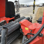 Close-up of red industrial machinery with black rollers and hoses on a construction site.