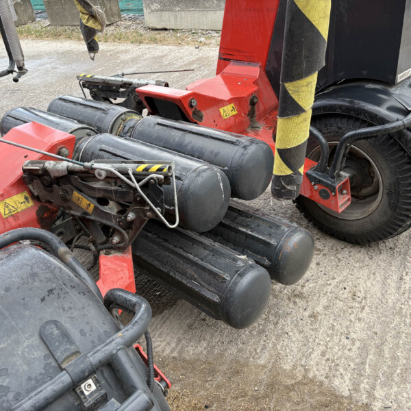 Red agricultural/industrial machine with large black tires and yellow-black warning stripes; close-up of hydraulic components and hoses on a dirt surface