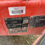 Close-up of a red agricultural machine with a white barcode sticker reading SW4014 and a black metal plate from KUHN-GELDROP B.V. attached.