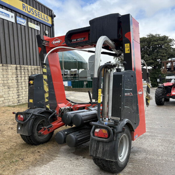 Red KUHN SW 4014 agricultural machine parked beside a dark building with a yellow Russell’s sign in the background.