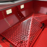 Close-up of a red metal interior with perforated steps, a vertical measurement scale on the left, and a yellow tool on the right side of the frame.