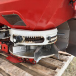 Close-up of red industrial machinery on a wooden pallet, showing a round gauge and rusted metal components beneath.