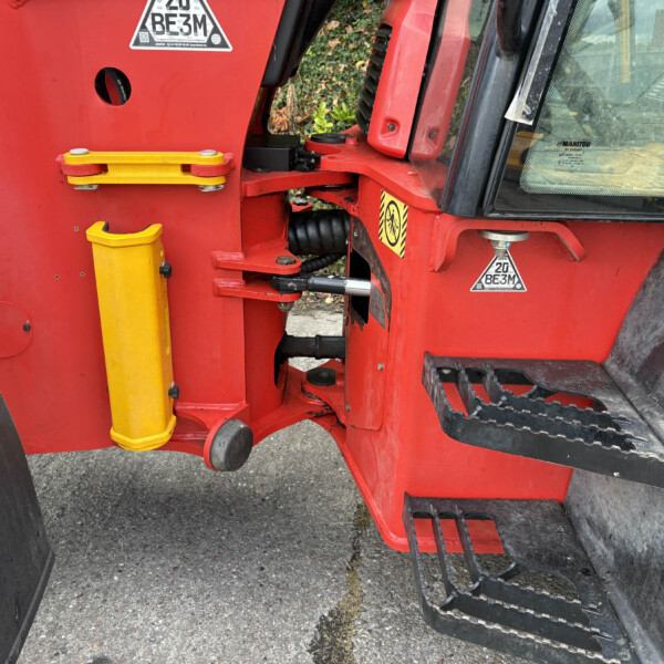 Close-up of red construction vehicle showing a yellow stabilizer leg and heavy black treaded wheel. Practical machinery details and hydraulic components visible.