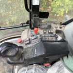 Close-up of a dusty tractor cabin control panel with multiple levers, switches, and a red joystick in the foreground.