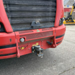 Close-up of the red truck front showing the grille, bumper, and tow hitch with yellow construction machinery visible in the background.