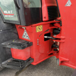Close-up of red heavy machinery with black step treads, warning labels, and vent grill.