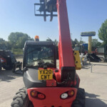 Rear view of a red Manitou telehandler with large tires and yellow plate XY20 CWT in a yard of farm equipment.
