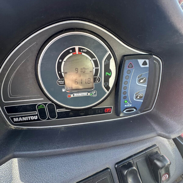 Dashboard cluster with analog RPM gauge and a rectangular digital display showing vehicle data, surrounded by control buttons on the steering console panel.