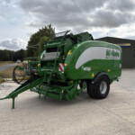 Green agricultural baler parked outside a metal warehouse with a Russell's sign on the wall.