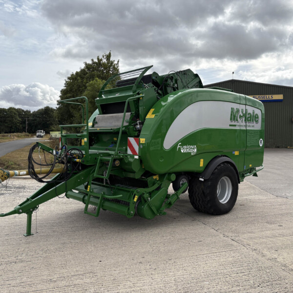 Green agricultural baler parked outside a metal warehouse with a Russell's sign on the wall.