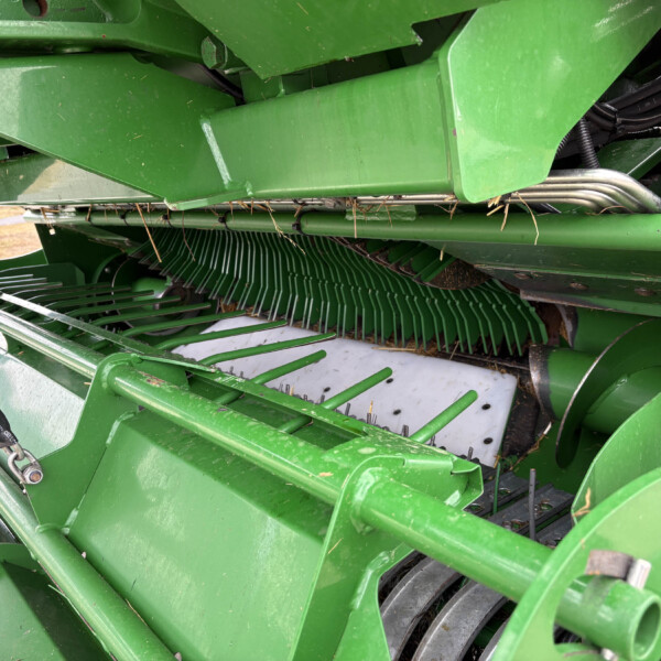 Close-up of green agricultural machinery showing metal blades and hydraulic hoses used for harvesting request.