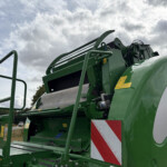 Close-up of a green agricultural header/harvester machinery with metal guards and yellow safety stickers against a cloudy sky.