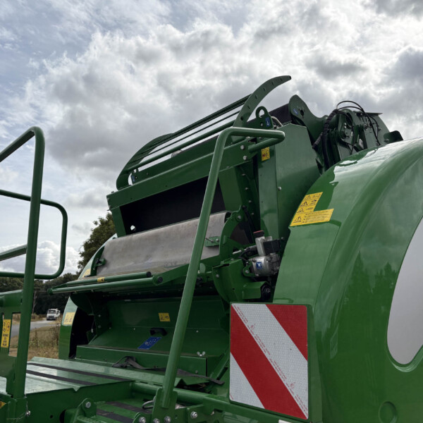 Close-up of a green agricultural header/harvester machinery with metal guards and yellow safety stickers against a cloudy sky.