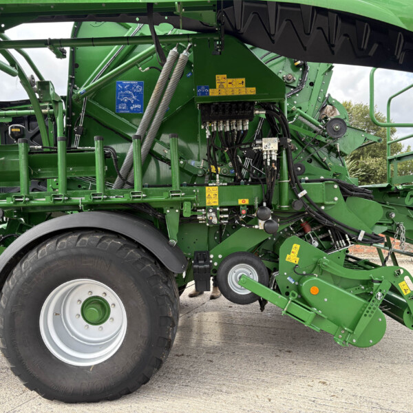 Close-up of a green agricultural machine with large wheels, hydraulic hoses, and metal framework (part of a planter/harvester).