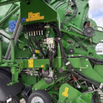 Close-up of green farming equipment showing hoses, belts, and warning stickers on an industrial machine outside.