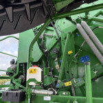 Close-up of green agricultural machinery with hydraulic hoses, metal brackets, and warning stickers on the frame.