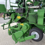 Close-up of green agricultural machinery showing hydraulic components, warning decals, and a large tire on the right side