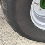 Close-up of a large tractor tire with a green wheel hub and bolts, resting on a rough concrete surface.