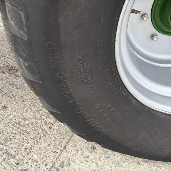 Close-up of a large tractor tire with a green wheel hub and bolts, resting on a rough concrete surface.