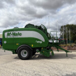 Green McHale Fusion baler parked in a lot under a cloudy sky, with flagpoles in the background.