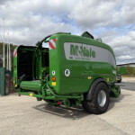 Green McHale baler in a parking lot, with other equipment and a cloudy sky in the background.