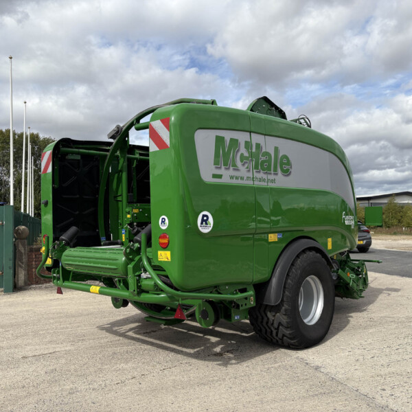 Green McHale baler in a parking lot, with other equipment and a cloudy sky in the background.