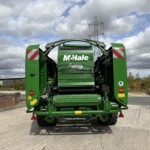 Rear view of a green McHale Fusion3 baler in a parking lot, with a cloudy sky and power lines in the background.
