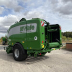 Rear view of a large green McHale baler parked in a lot under a cloudy sky with power lines nearby