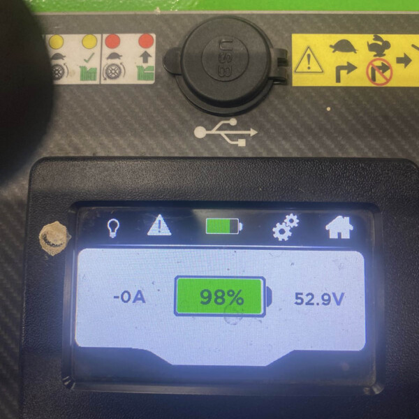 Close-up of a handheld diagnostic screen showing 98% battery, 52.9V, and USB icon with safety warning stickers above on a green and gray panel.