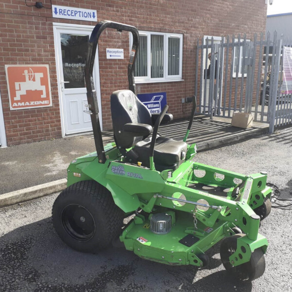 Green riding lawn mower parked outside a brick building near a reception sign.