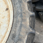 Close-up of a muddy tractor tire with a dusty white rim and dirt on the sidewall, showing rugged tread patterns.