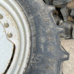 Close-up of a muddy tractor tire with a knobby tread beside a white, rusted wheel rim.